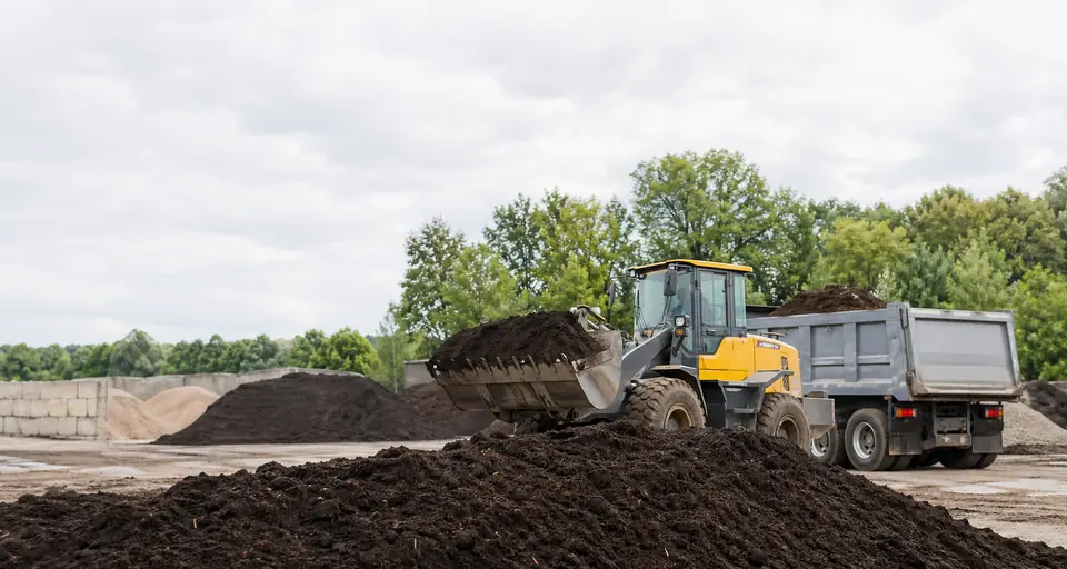 Topsoil piles at a local material yard with a loader and truck